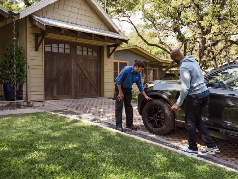 image of a man looking at the tire on a car in a driveway
