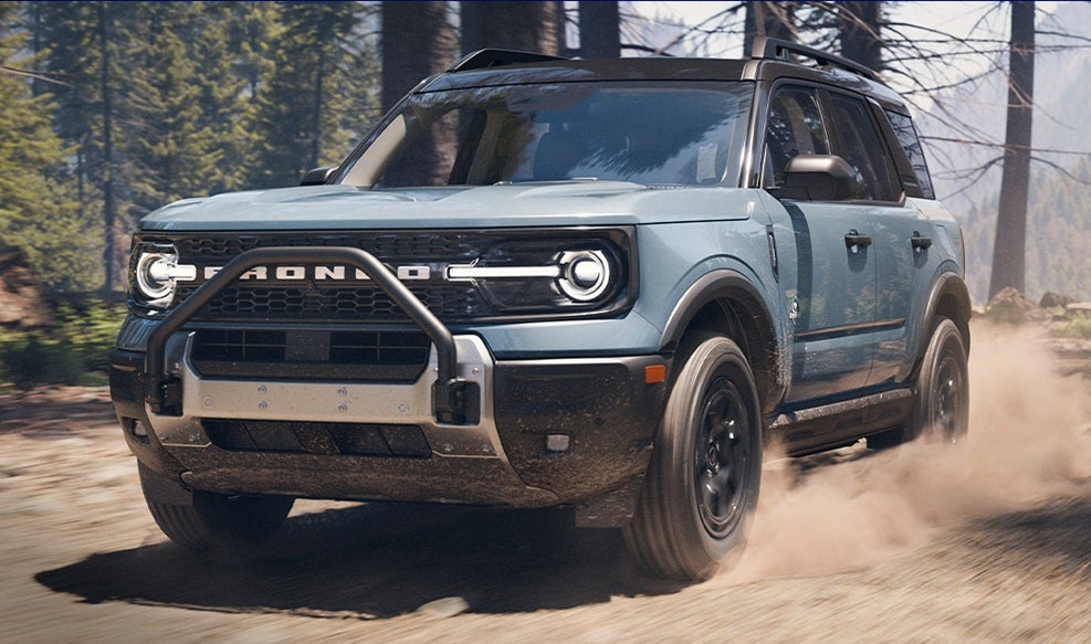 Light blue Ford Bronco Sport traveling in a wooded area on a sunny day