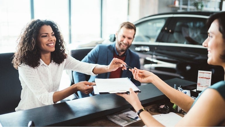 image of a woman receiving a key at a car dealership with a man sitting next to her
